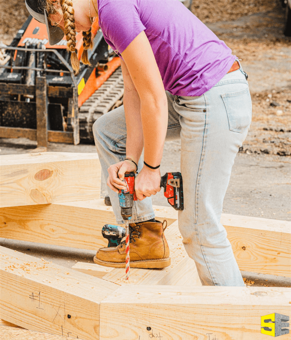 A person, using a drill to connect pieces of wood into a frame