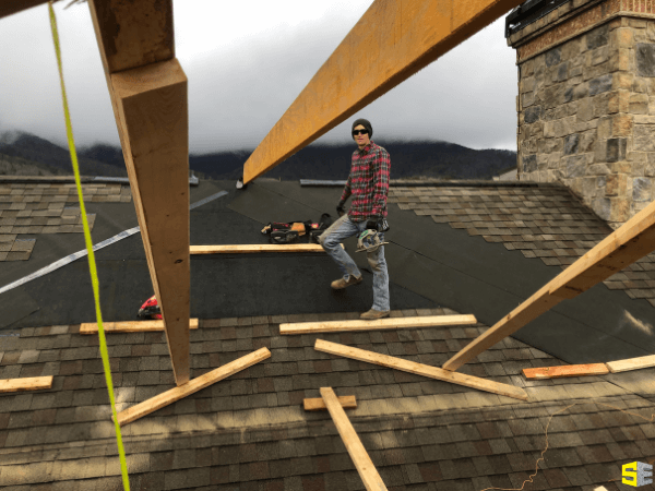 Image focuses on a person, working on adding shingles to a roof of a commercial building