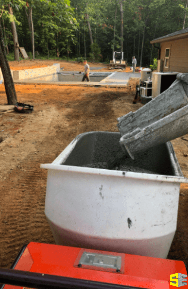 A machine pouring concrete as a person works on the construction site behind them