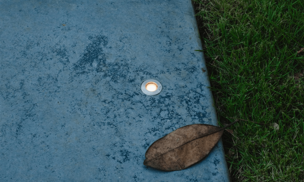 A light tucked into a concrete pathway with a leaf laying beside it