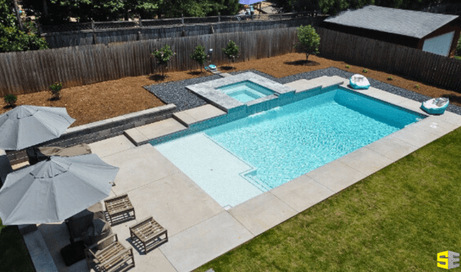 A finished residential in ground pool site with concrete surrounding it