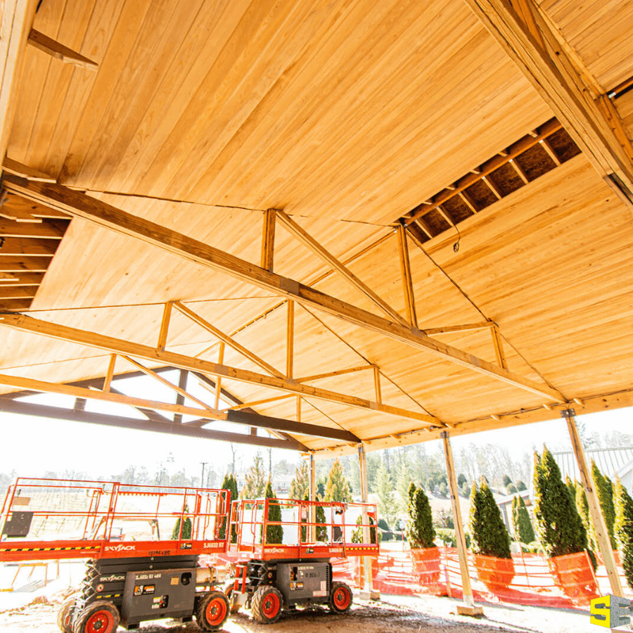 Framing done to the underside of a roof of an outdoor building with two lifts in the background