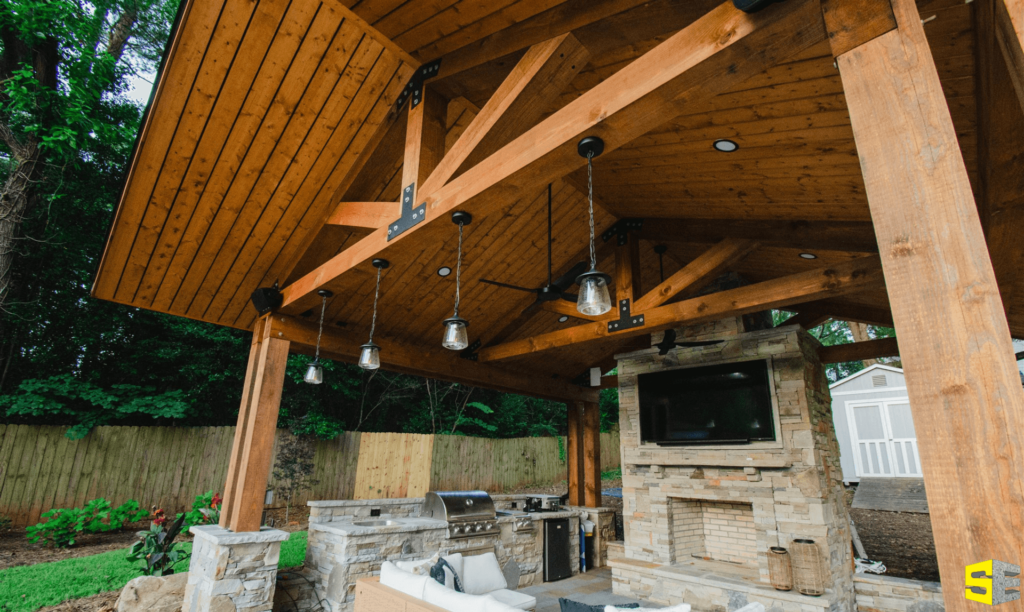 An outdoor living space with a fireplace as the centerpiece, a grill off to the side and lights hanging from the post of a roof