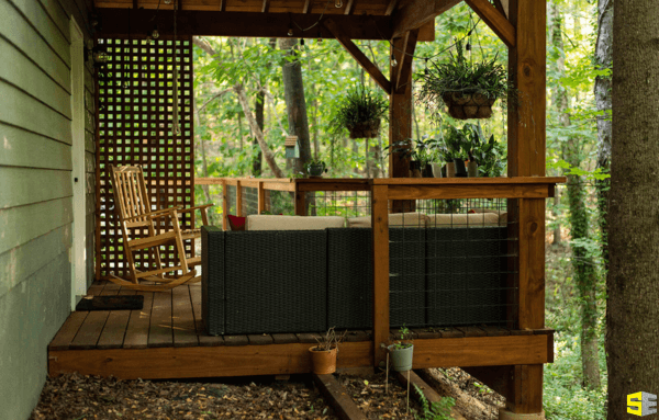 An outdoor patio in the middle of the woods, featuring a rocking chair and an outdoor couch