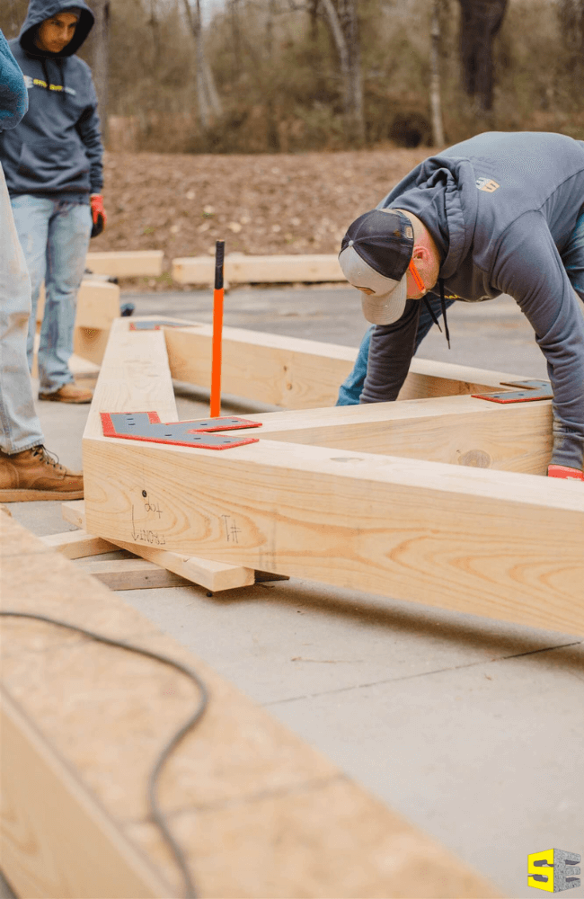 Two people working on the frame for an outdoor building