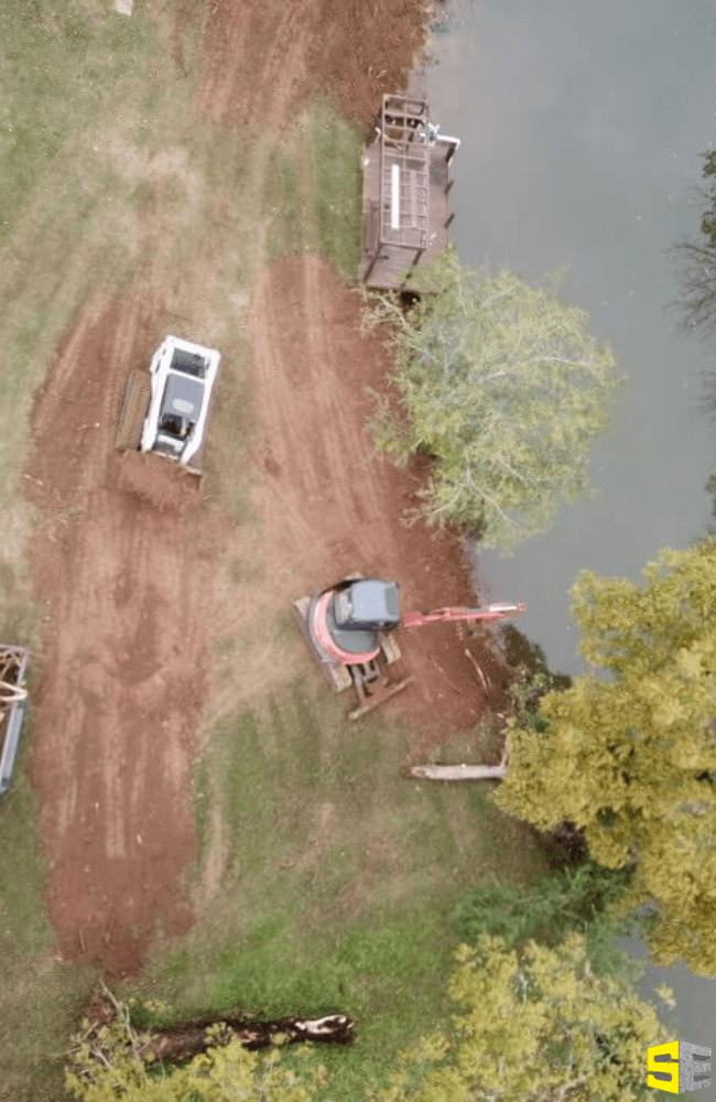 A crane and a tractor working on a construction site landscaping beside a man made lake