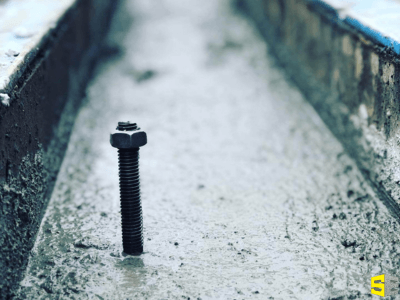 A screw with a washer on top stuck into drying concrete.