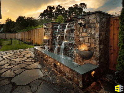 A stone water feature, with both warm lamp lighting and fire features just beneath the lamps.