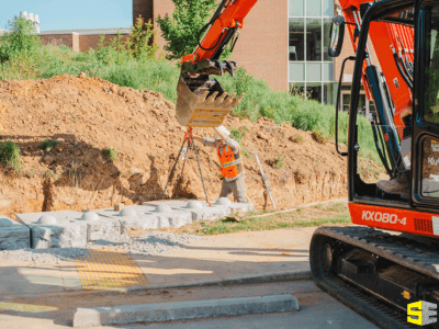 A person guiding a crane down to place stones on a retaining wall