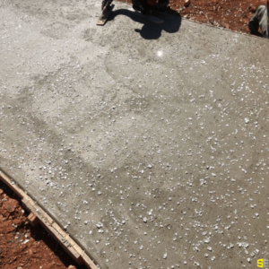 A worker smoothing out freshly poured concrete with decor sprinkled on top of it