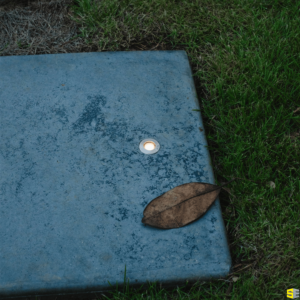 A finished concrete stone with an embedded outdoor light, a leaf to the side of it