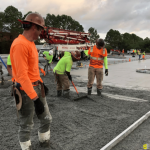 On a construction site, a group of workers smooth out concrete on a surface