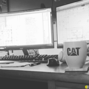 A cup of coffee in front of two monitors displaying blueprints