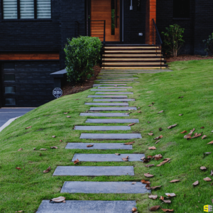 A concrete walkway, leading up to a residential home with soft lighting underneath the steps