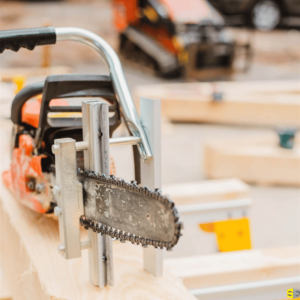 A close up of a chain saw leaning against multiple pieces of freshly cut construction planks