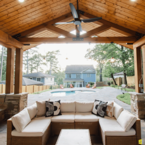 A backyard gazebo area with outdoor furniture, looking out to an inground pool surrounded by concrete walkways