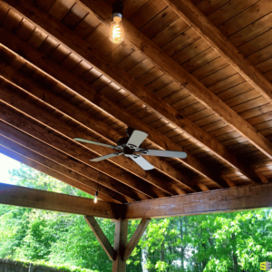 A look at a ceiling fan, mounted to the wood ceiling of an outdoor gazebo