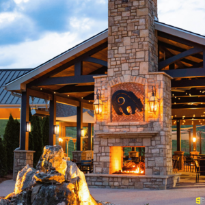 A photo focusing on a stone made fireplace, a concrete carved bear at the hearth and a fire lit beneath it