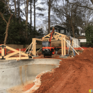 The frame work of an outdoor gazebo being built by a crane and a construction worker