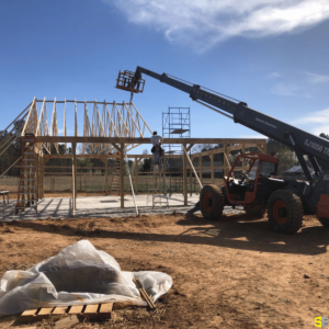 A construction worker, standing on a ladder beside a crane, working to build a frame for an outdoor gazebo