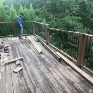 A wooden outdoor deck being constructed, the top pieces to railings being fitted by a construction worker