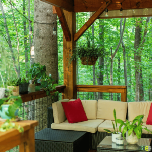 The finished product of an outdoor patio, with outdoor furniture, surrounded by hanging plants and the forest