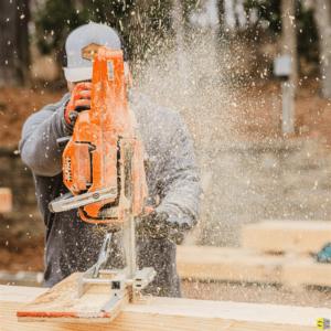 A construction worker using a saw to cut apiece of wood on a construction site