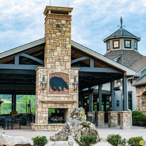 A close up of an outdoor gazebo attached to a side building, a stone fireplace with a concrete carving of a bear on the hearth