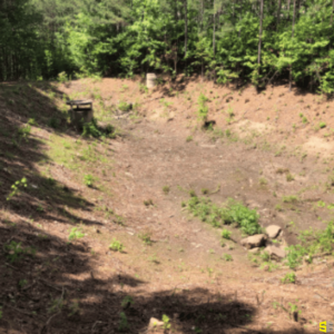 A man made drainage area to the side of a dirt road