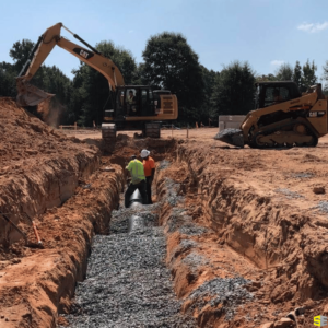 Two workers burying a large drainage pipe