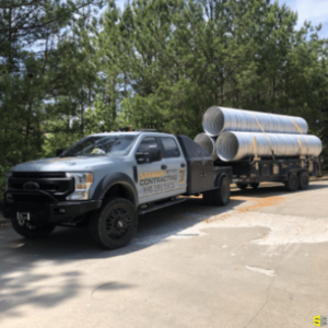 A Straight Edge pickup truck towing three large drainage pipes