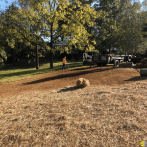 A construction worker using a rake to flatten out the dirt of a finished project