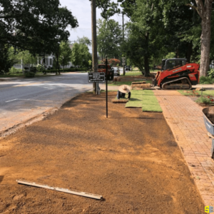 A worker rolling out carpet grass on freshly tilled ground