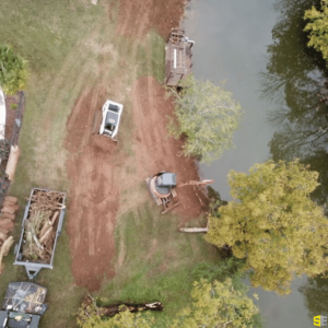 A tractor and crane working to flatten out land beside a lake