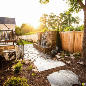 A concrete walkway, leading up to a backyard porch and a concrete water feature