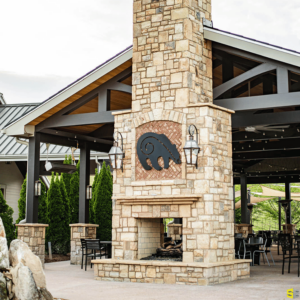 A stone, outdoor fireplace, with a concrete carving of a bear placed at the hearth