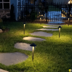 A concrete walkway illuminated by small mushroom like outdoor lights on the sides