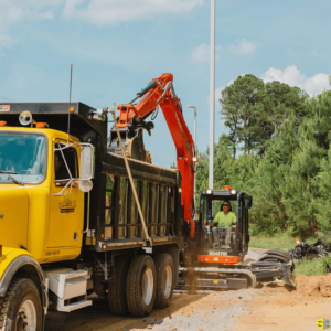 A worker, using a crane to dump top soil into the back of a dump truck