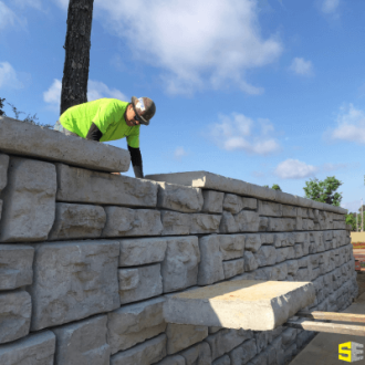 Person working on a stone retaining wall, placing the last stones on the top for completion.